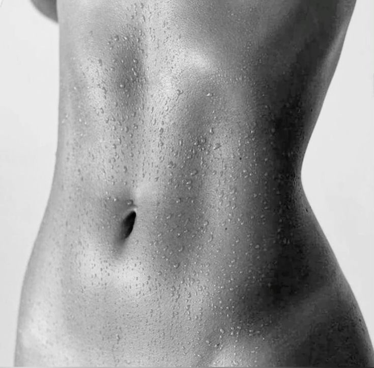 Black and white image of a person's wet torso with water droplets, showing the abdomen and part of the chest.